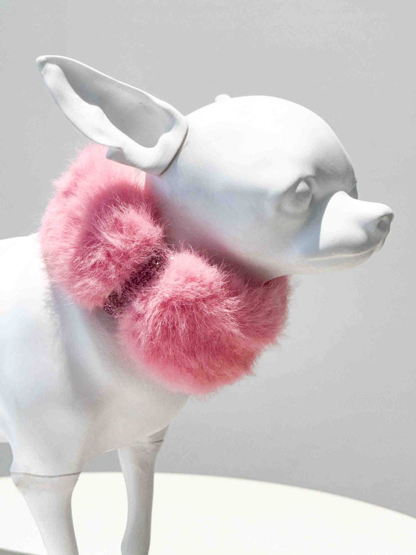 A luxurious pink fur dog collar adorned with sparkling rhinestones, displayed on a white dog mannequin, showcasing a stylish and elegant accessory for pets.
