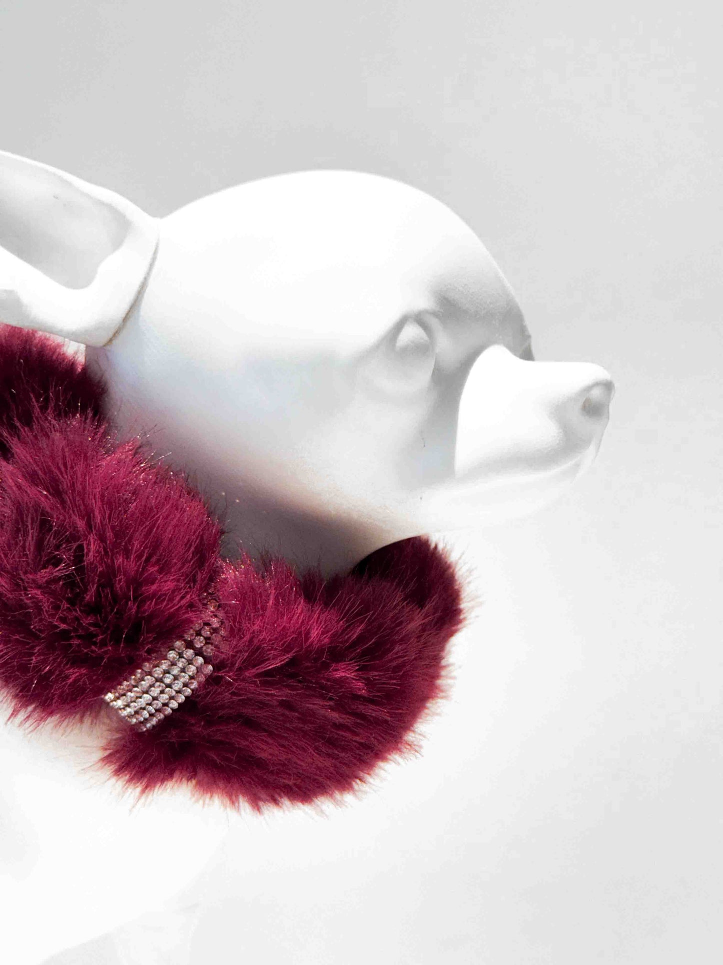 A luxurious red fur dog collar adorned with sparkling rhinestones, displayed on a white dog mannequin, showcasing a stylish and elegant accessory for pets.